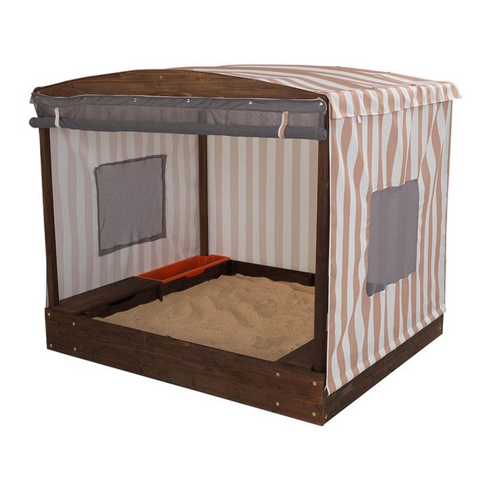 A wooden sandbox with a striped canopy sits on the ground, featuring a sandy interior and a small orange storage tray inside.