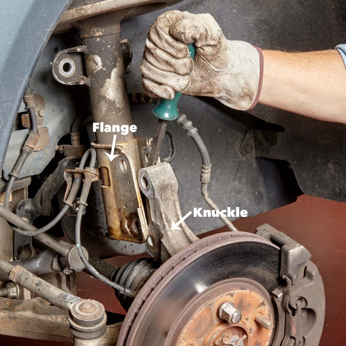 A hand wearing a glove uses a screwdriver to adjust components labeled "Flange" and "Knuckle" on a vehicle's suspension system against a dark background.