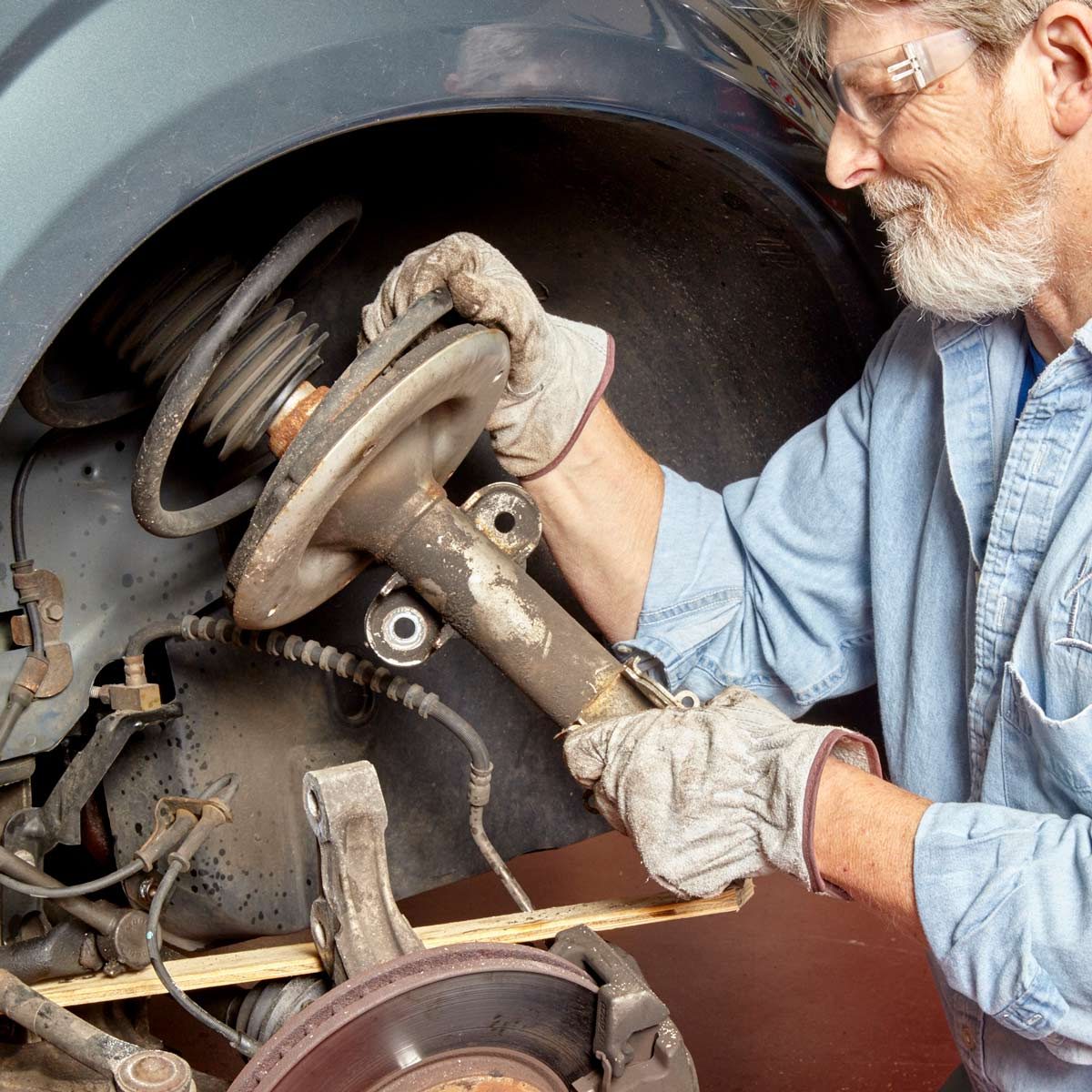 A man in gloves works on a car's suspension, removing a part near the brake assembly inside a garage.