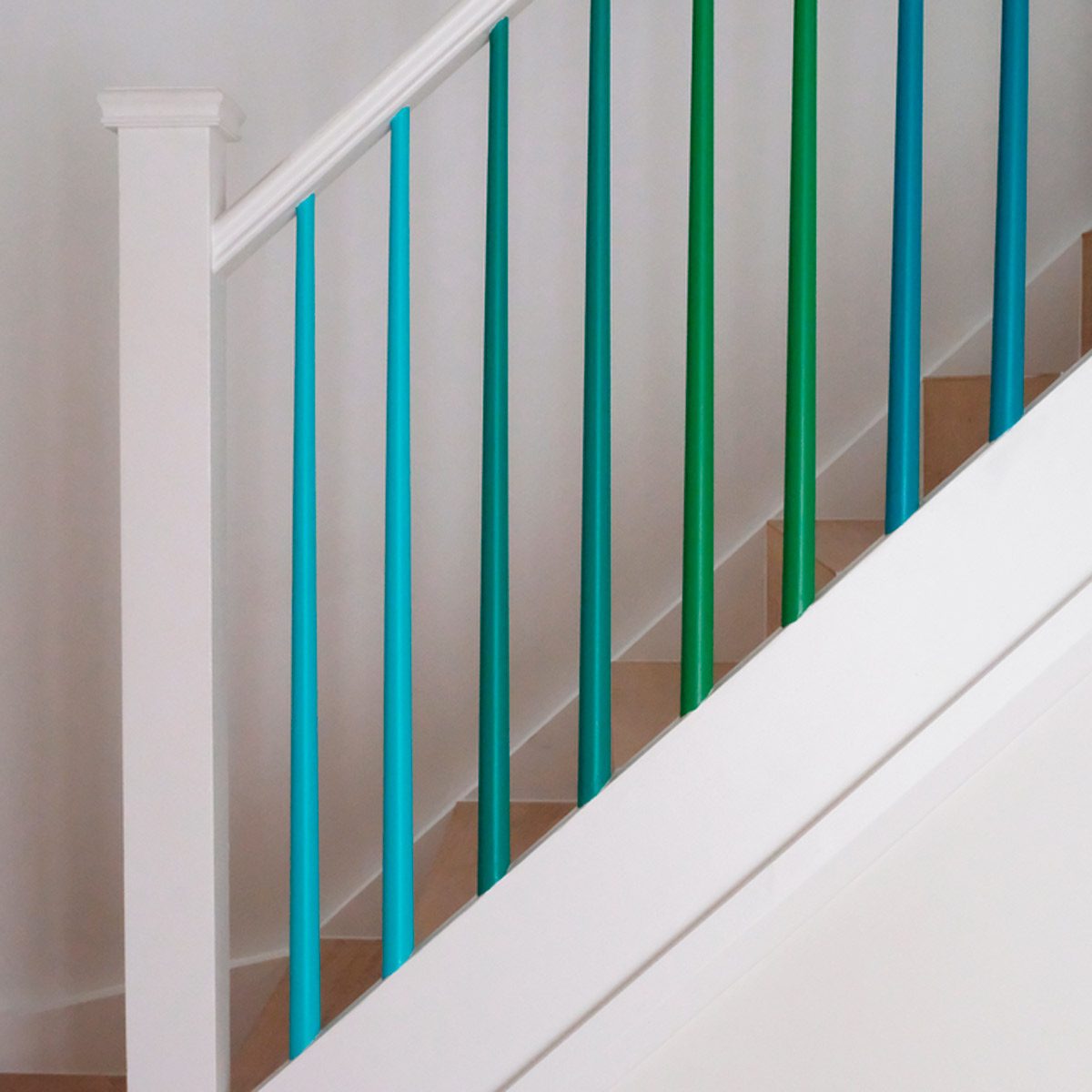 Colorful vertical railings ascend a white staircase, providing safety while contrasting with the wooden steps and light wall, creating a modern interior aesthetic.
