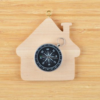 A compass rests on a wooden house-shaped base, with a hook above it, set against a light wooden background.