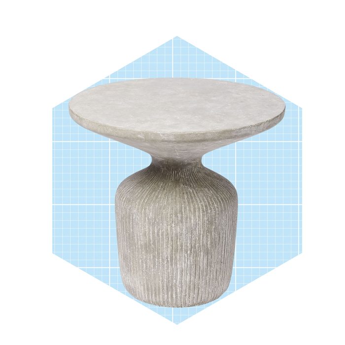 A round, stone-like side table stands with a flared top, textured cylindrical base, set against a light blue grid background.