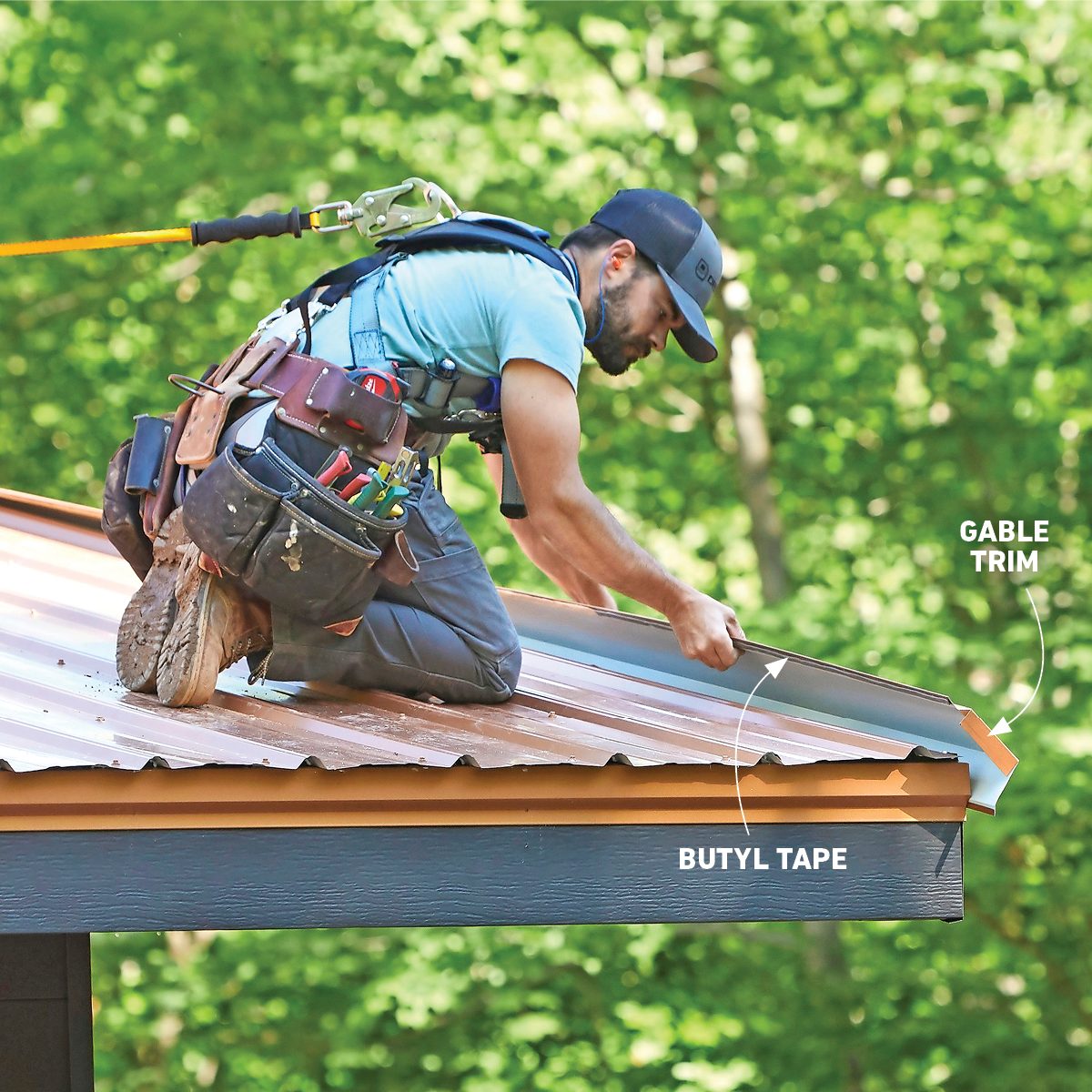 A worker kneels on a roof, applying gable trim with butyl tape, surrounded by green trees in a clear, outdoor setting.