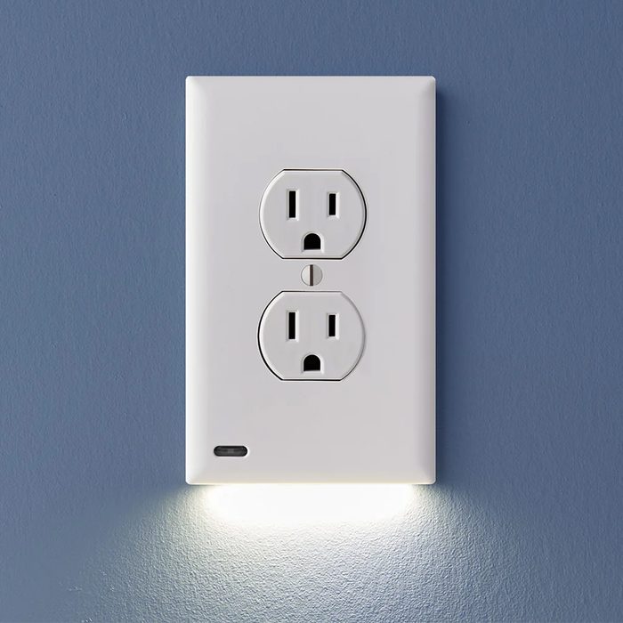 A white electrical outlet with two sockets is mounted on a blue wall, featuring a small LED light glowing underneath.